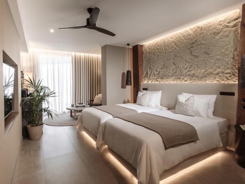 Camera d'hotel moderna con due letti, illuminazione indiretta e grande finestra.