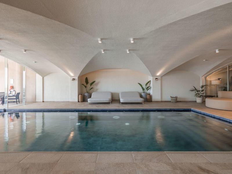 Piscina interna con luce naturale, pareti bianche, divani e piante in un'elegante area spa.