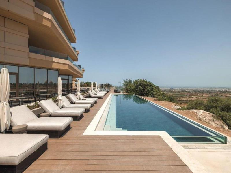 Piscina a sfioro moderna con lettini e vista sul paesaggio.