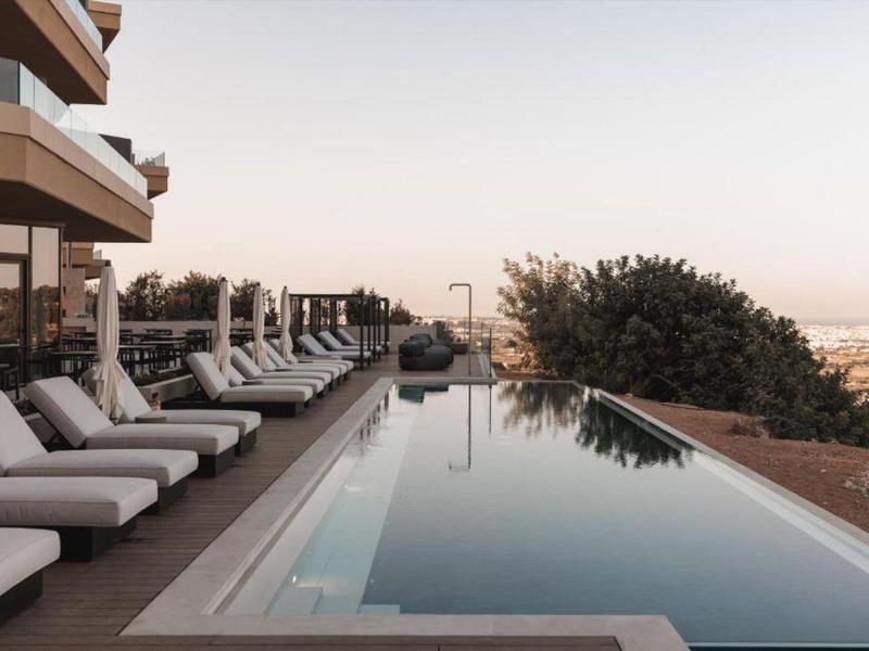 Piscina moderna con lettini, vista sulla città e alberi sullo sfondo.