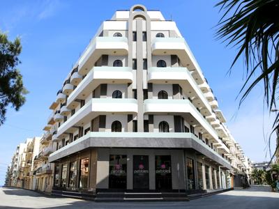 Moderní vícepatrový hotel s bílými balkóny pod jasnou modrou oblohou.