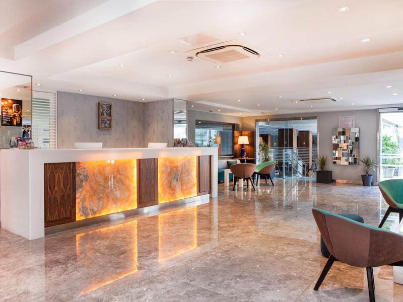 Světlá, moderní hotelová lobby s osvětlenou recepcí a posezením.