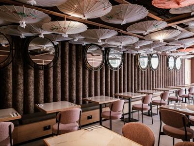 Elegancka restauracja z brązowymi krzesłami, drewnianymi stołami i dekoracyjnymi okrągłymi lustrami na ścianie.