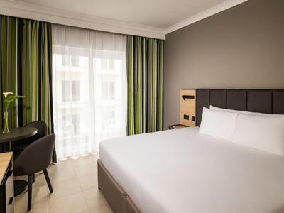 Chambre d'hôtel moderne avec grand lit, bureau et balcon avec rideaux.