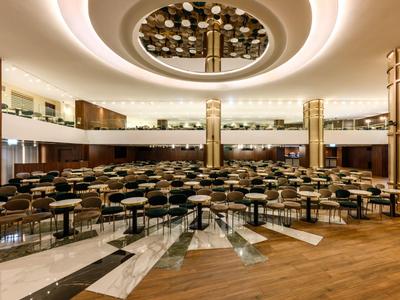 Grande salle de conférence avec rangées de chaises, lumière de plafond ronde et balcon sur deux étages.