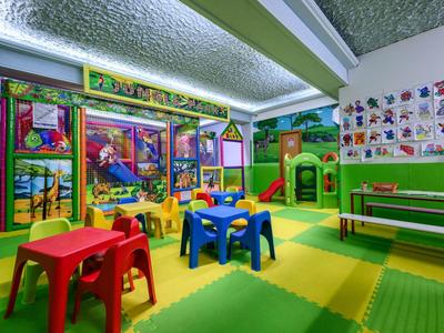 Aire de jeux intérieure colorée avec structure d'escalade, petites tables et chaises dans une salle adaptée aux enfants.