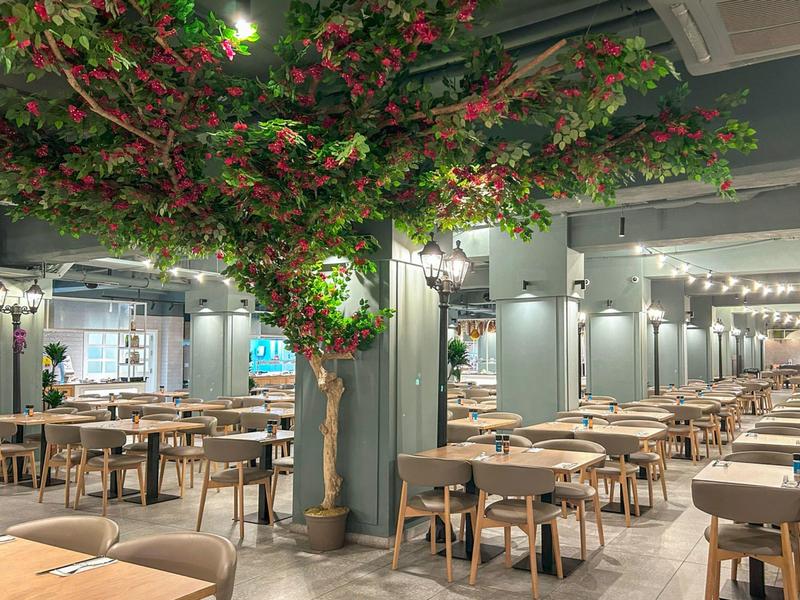 Grand restaurant avec de nombreuses tables et chaises en bois et un grand arbre au centre.