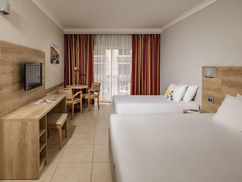 Chambre d'hôtel avec deux lits, télévision murale et petite table avec chaises près de la fenêtre.