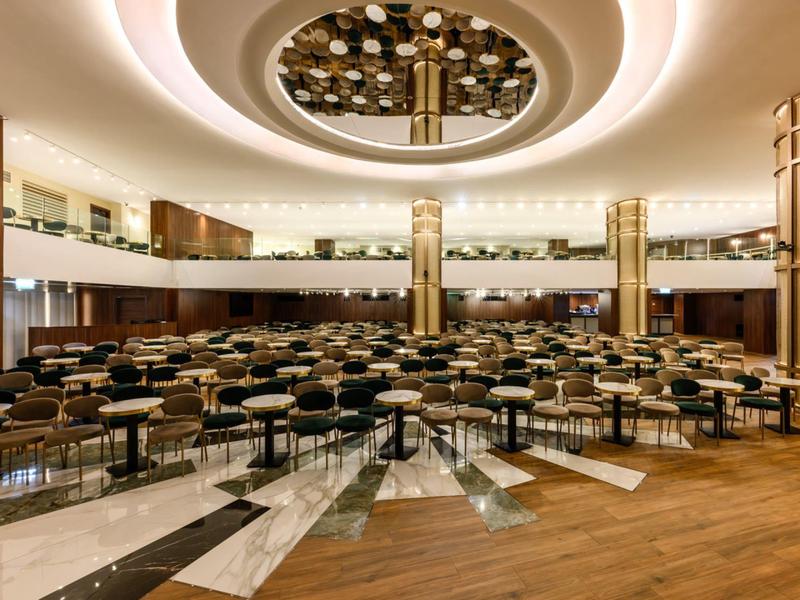 Grande salle de conférence avec rangées de chaises, lumière de plafond ronde et balcon sur deux étages.