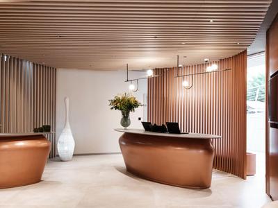 Réception d'hôtel moderne avec comptoir courbe couleur cuivre et panneaux en bois.