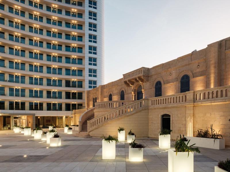 Extérieur d'un hôtel avec un bâtiment moderne et un bâtiment traditionnel au coucher du soleil.