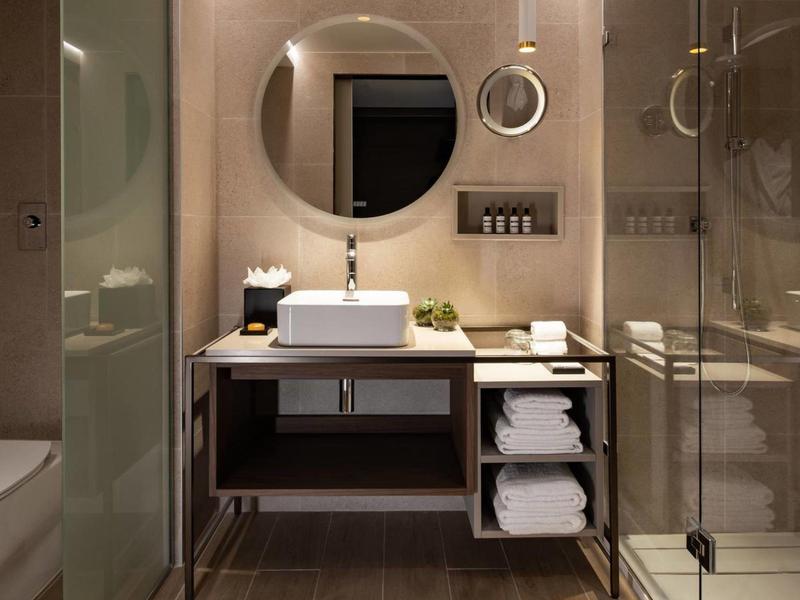 Salle de bain moderne avec lavabo, miroir rond et douche en verre.