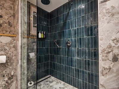 Zone de douche avec carrelage bleu foncé et murs en marbre dans une salle de bain.