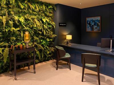 Hall d'hôtel moderne avec mur végétal, deux chaises et comptoir d'accueil sous lumière chaude.