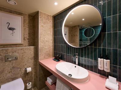 Salle de bain moderne avec miroir rond éclairé, lavabo plat et plan de travail rose.