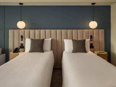 Chambre d'hôtel moderne avec deux lits simples et des lampes suspendues chaudes sur un mur sombre.