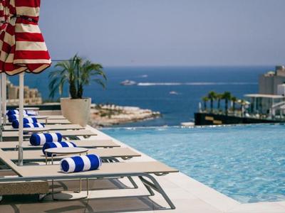 Poolbereich mit Liegestühlen, Sonnenschirmen und Blick auf das Meer.