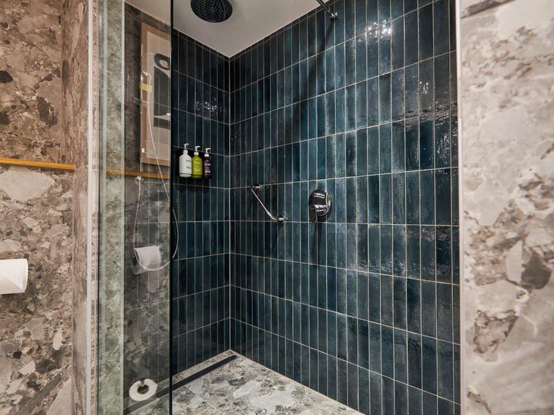 Zone de douche avec carrelage bleu foncé et murs en marbre dans une salle de bain.