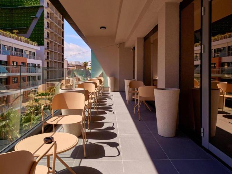 Balcon moderne avec tables et chaises donnant sur des bâtiments urbains sous le soleil.