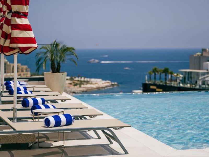 Espace piscine avec transats, parasols et vue sur la mer.