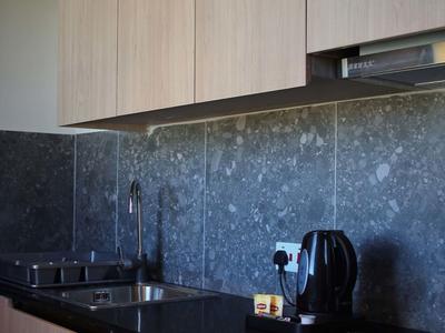 Moderní kuchyně se dřevěnými skříňkami, černými pracovními deskami a šedým mramorovým obkladem.