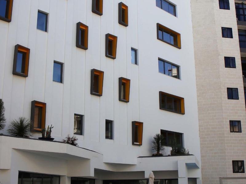 Modern hotel building with white walls and small rectangular windows with brown frames.