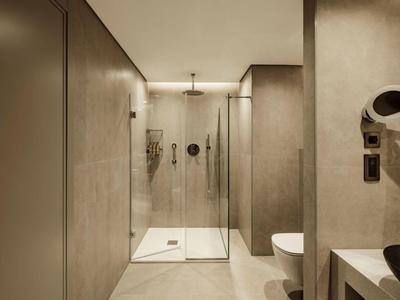 Nowoczesna, minimalistyczna łazienka hotelowa z przeszklonym prysznicem typu walk-in i minimalnymi dodatkami.