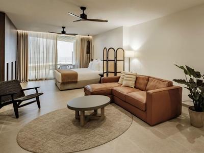 Modern eingerichtetes Hotelzimmer mit Bett, Sofa, Sesseln und großem Fenster.