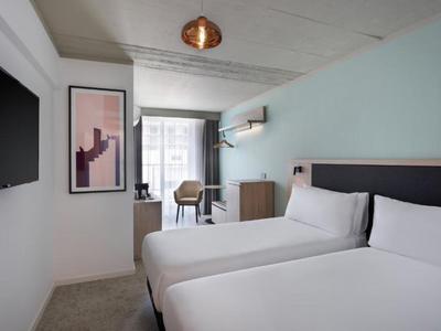 Camera d'hotel con due letti, TV, scrivania e finestra con vista sulla città.