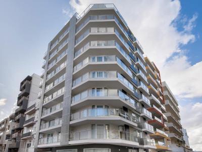 Edificio residenziale moderno su più piani con balconi e ringhiere in vetro sotto un cielo azzurro.