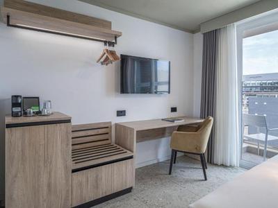 Area moderna della camera d'hotel con scrivania, sedia, TV e balcone con vista esterna.