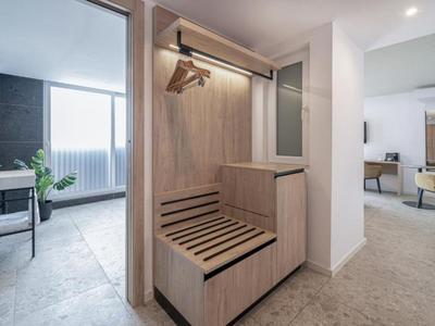 Corridoio con appendiabiti in legno e ganci accanto a un soggiorno luminoso.