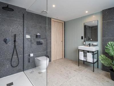 Bagno moderno con pareti in pietra grigia, doccia a filo pavimento e arredi minimalisti.