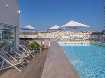 Piscina sul tetto di un hotel con lettini e ombrelloni sotto un cielo limpido.