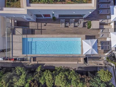Vista aerea di una piscina rettangolare con ombrellone e terrazza in legno, circondata da alberi.