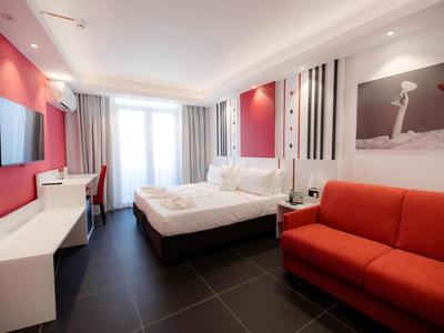 Camera d'hotel moderna con letto matrimoniale, divano rosso e TV a parete.