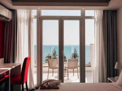 Camera d'hotel con vista mare attraverso grandi finestre e due sedie sul balcone