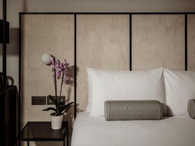 Camera moderna con letto bianco, cuscini grigi, comodino e orchidea viola.