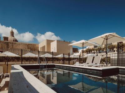 Area piscina di un hotel moderno con lettini, ombrelloni e cielo limpido sullo sfondo.