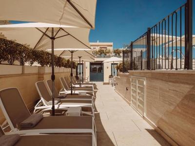 Terrazza solarium con lettini e ombrelloni sul tetto di un hotel sotto un cielo limpido.