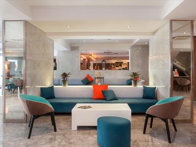 Modern eingerichteter Hotel-Lobby-Bereich mit Sofa, Sesseln und dekorativen Kissen.