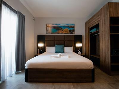 Modernes Hotelzimmer mit großem Bett, dunklem Holzmöbel und hellem Vorhang am Fenster.