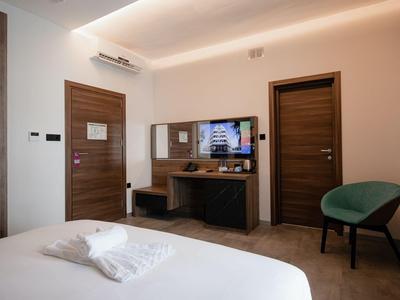 Modernes Hotelzimmer mit Doppelbett, Schreibtisch, Fernseher und grünem Sessel.