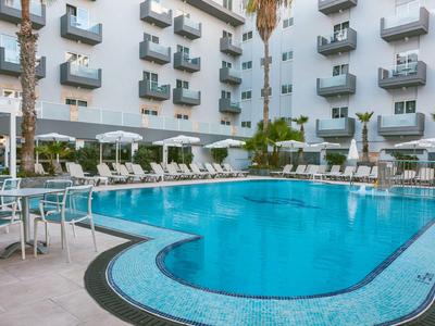 Hotel mit Außenpool, Sonnenliegen und weißen Gebäuden mit Balkonen.