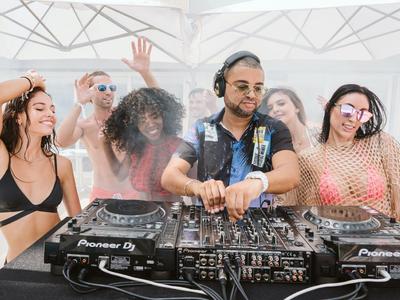 DJs und tanzende Menschen genießen Musik unter einem weißen Sonnenschutz.