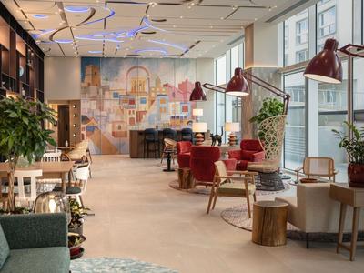 Moderner Hotel-Loungebereich mit bequemen Stühlen, hängenden Lampen und großer Fensterfront.