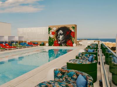 Dachpool mit Liegestühlen und Getränken, Wandkunst im Hintergrund, Meerblick.