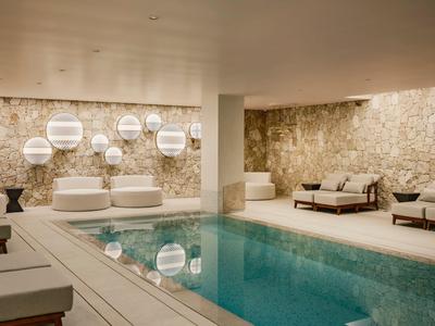 Moderner Innenpool mit Steinwand, beleuchteten Dekoelementen und Liegen im Wellnessbereich.