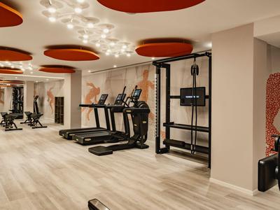 Moderner Fitnessraum mit Laufbändern, elliptischen Geräten und Hantelstation in neutralem Farbschema.