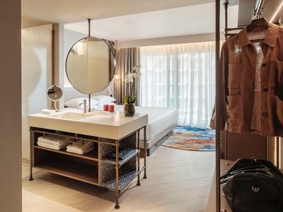 Modern eingerichtetes Hotelzimmer mit Waschbecken, Spiegel und Garderobe mit Jacke und Koffer.